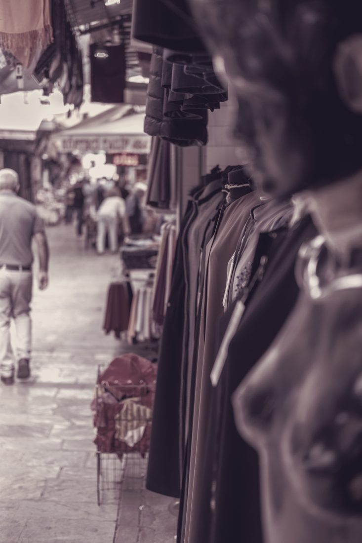 Market aisle with rails of jackets and shirts, shoppers in the background