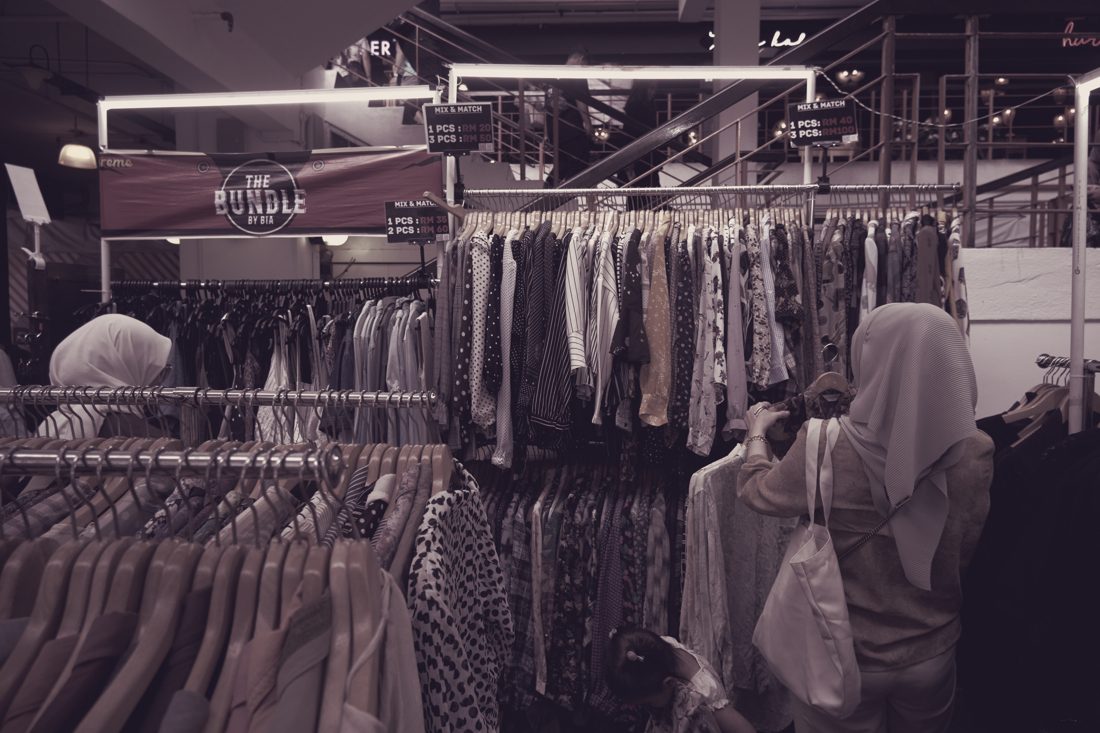 Shopper with headscarf and shoulder bag between rails of clothing at a market